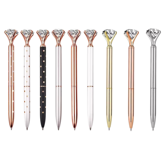 Ballpoint pens with diamond-shaped tops arranged side by side on a white background. Designs include rose gold, gold, silver, black with gold polka dots, white with rose gold polka dots, and solid white and metallic finishes.
