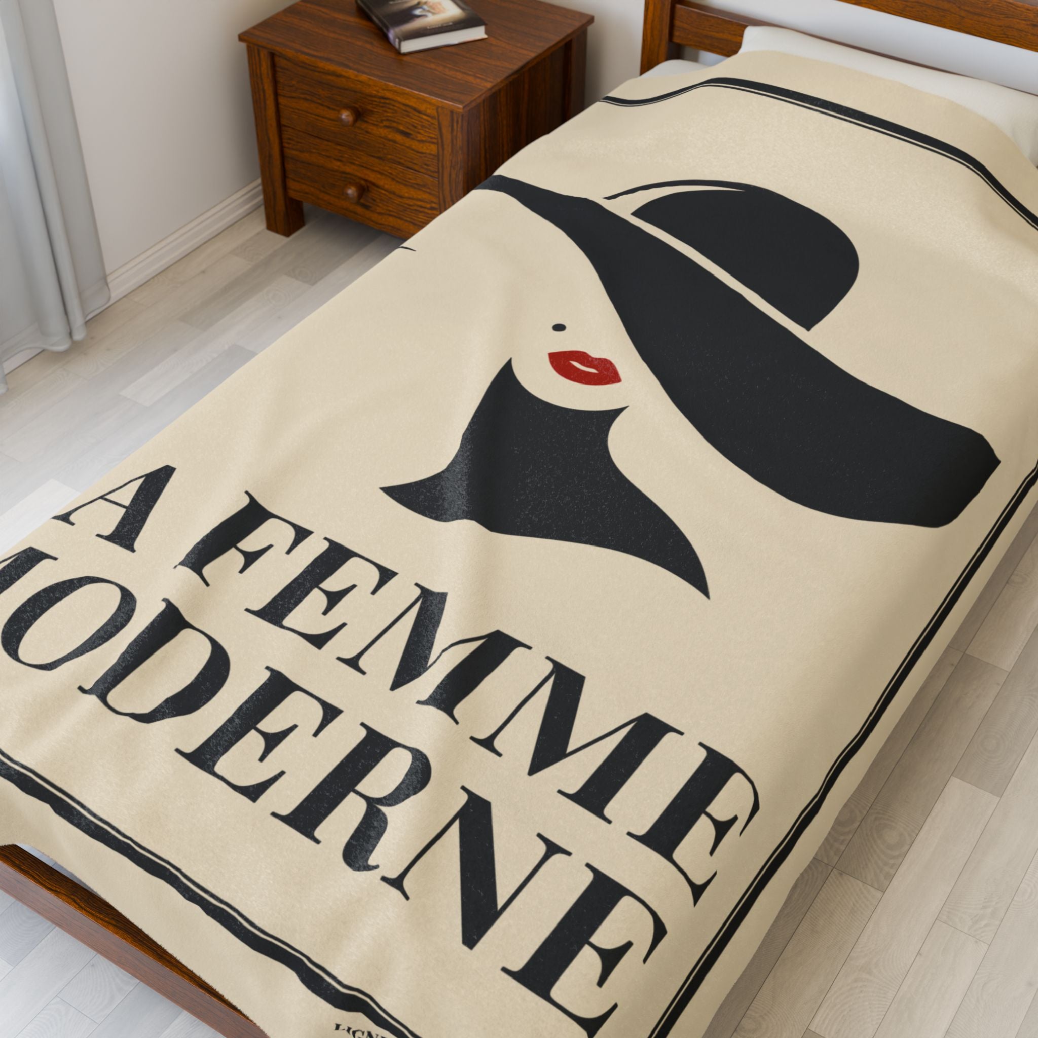 Blanket with a graphic design of a woman's face and the text 'A Femme Moderne' on a bed.