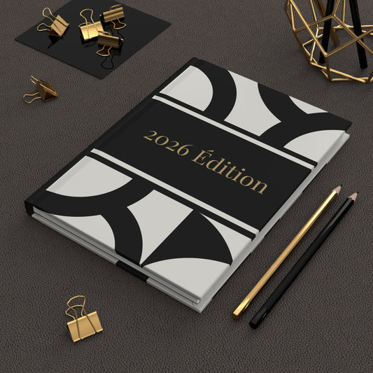 2026 Edition hardback notebook with decorative cover on a dark surface with office supplies.
