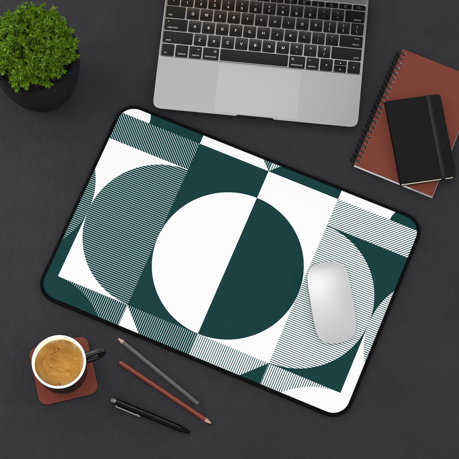 Desk setup with a geometric design mouse pad, laptop, notebook, and coffee cup.